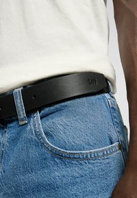 Black leather belt with a smooth finish, adjustable holes, and a rectangular buckle, worn over light blue denim jeans.