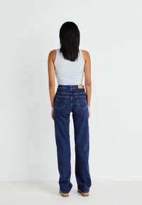 Blå høy midje jeans med avslappet passform, to baklommer og lys søm. Kombinert med en lys grå ermeløs topp.