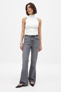 Valkoinen hihaton mock neck -paita, joka on yhdistetty harmaisiin leveälahkeisiin farkkuihin. Asusteena on musta vyö ja terävät mustat kengät.