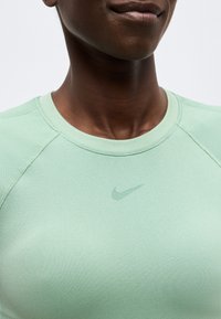 Κοντινό πλάνο ενός ατόμου που φοράει μπλούζα Nike ανοιχτού πράσινου χρώματος με μικρό λογότυπο Nike στη μέση του στήθους.