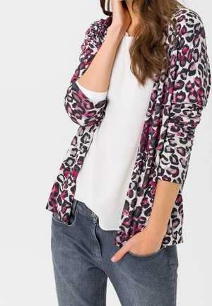 Svetr s leopardím vzorem v růžové a černé barvě přes bílý top, vyrobený z lehké látky s dlouhými rukávy a otevřeným předním dílem.