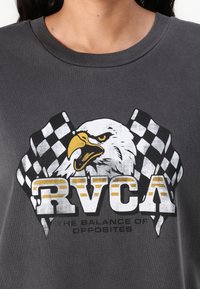 Grå bomull T-skjorte med et fremtredende grafikk av en ørn med racerflagg. Teksten leser "RVCA" og "BALANSEN AV MOTSETNINGER."