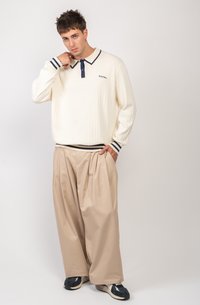 Polo de manga larga con canalé en crema y ribetes en marino, combinado con pantalones beige de corte oversize. Zapatillas casuales completan el conjunto.