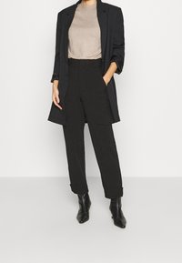 Czarne dopasowane spodnie z ukośnymi kieszeniami, zestawione z jasnobeżową bluzką i ciemną marynarką. Czarne botki na ostrym czubku dopełniają stylizację.