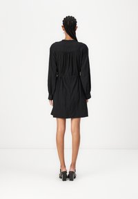Rochie neagră, cu mâneci lungi, cu talie elastică, dintr-un material texturat și cu o margine puțin evazată. Prezintă un decolteu rotund și o croială lejeră.