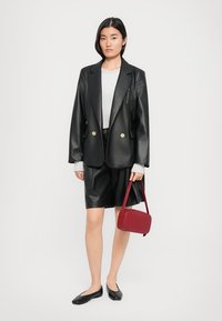 Svart blazer i faux skinn med gullknapper, grå genser, svarte shorts i faux skinn, svarte ballerinsko og en liten rød håndveske.