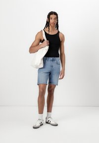 Top negru fără mâneci, pantaloni scurți din denim de un albastru deschis, adidași gri și albi, ținând o geantă tote crem. Design minimalist, cu o croială casual.