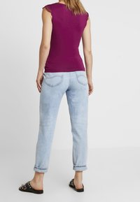 Top morado ajustado sin mangas con mangas de encaje, combinado con jeans azul claro de puño vuelto y sandalias negras planas con tachuelas.