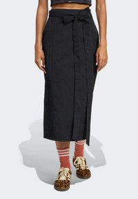 Czarna midi spódnica z wiązaniem w talii, charakteryzująca się pionowymi szwami i teksturowanym materiałem. Połączona z brązowymi trampkami w panterkę i pasiastymi skarpetkami.