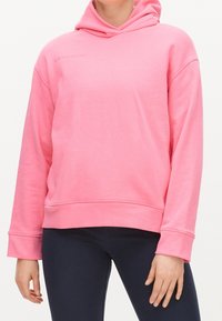 Růžová bavlněná mikina s volným střihem, velkou kapucí, žebrovanými manžetami a značkovým logem na hrudi. Hladká textura a neformální design.
