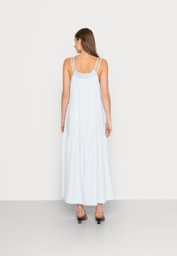 Vestido maxi azul claro com corpete franzido, alças finas e saia em camadas. Apresenta um corte relaxado e um tecido suave e fluido.