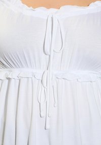 Valkoinen mekko, jossa on olkaimeton kaula-aukko, kerätty yläosa ja solmittava kiinnitys. Sisältää röyhelöreunan ja kevyen, sileän kankaan.