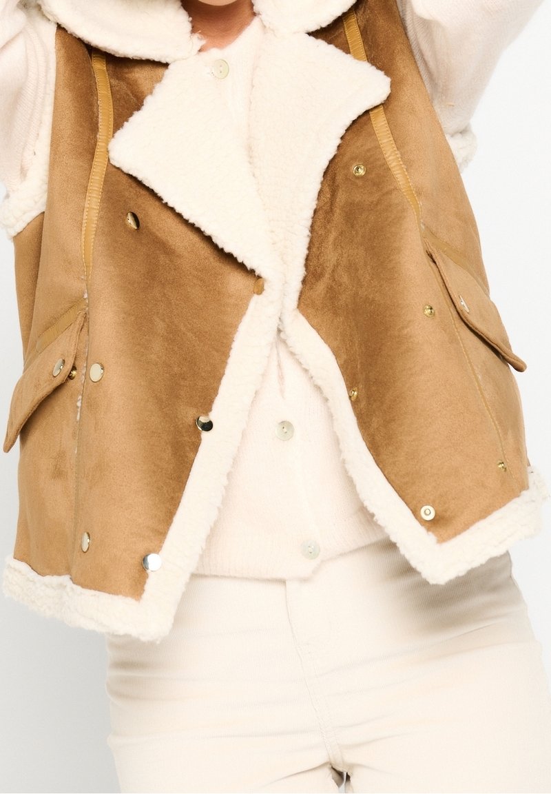 Hnědá faux suede vesta s bílým fleecovým podšívkou, má široký límec, patentky a dvě přední kapsy. Měkká textura a jednoduchý design.