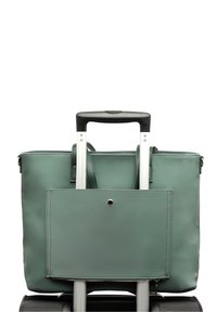 Roheline pehme reisikott, mis on kinnitatud musta veereva kohvri metallist teleskoopkäepideme külge, mis on välja tõmmatud.