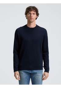 Maglione a maniche lunghe blu navy realizzato in tessuto morbido, con colletto rotondo e design semplice, abbinato a jeans blu chiaro.