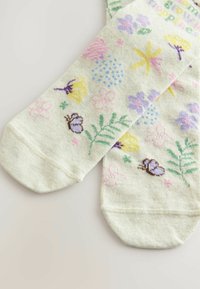 Vihreät sukat, joissa on kukkakuosi, jossa on violetteja, keltaisia ja vaaleanpunaisia kukkia, perhosia ja vihreitä lehtiä. Sukat on valmistettu pehmeästä kankaasta.