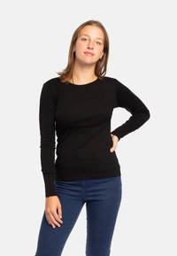 Maglietta nera a maniche lunghe con scollatura rotonda, design aderente e texture liscia, abbinata a jeans in denim blu.