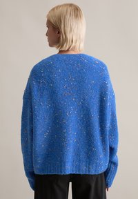 Blauer, strukturierter Pullover mit lockerem Schnitt, durchzogen von mehrfarbigen Sprenkeln. Lange Ärmel und ein rundes Halsbündchen vervollständigen das Design.