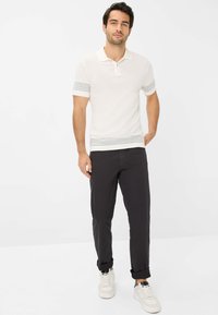 Lichtgekleurde polo met korte mouwen, met grijze horizontale strepen op de manchetten en de zoom. Gecombineerd met een donkere slim-fit broek en sneakers.