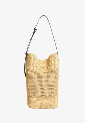 Gewebte beige Beuteltasche mit verstellbarem schwarzem Schultergurt, charakterisiert durch ein strukturiertes, offenes Gewebemuster und eine abgerundete, strukturierte obere Kante.