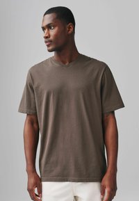 Tricou v-neck marron, fabricat din bumbac moale. Are mâneci scurte, o croială relaxată și detalii minimale de coasere.
