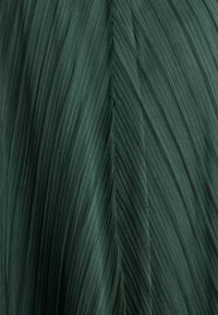 Tessuto plissettato di colore verde scuro, caracterizzato da linee verticali e una texture liscia. Il design presenta leggere ondulazioni e variazioni di ombreggiatura.
