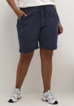 Pantalones cortos azul marino, hasta la rodilla, hechos de material ligero con una cinturilla con cordón y bolsillos laterales visibles. Detalles de dobladillo enrollado.