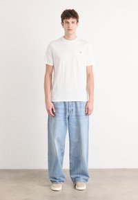 Weißes Baumwoll-T-Shirt mit kurzen Ärmeln, kombiniert mit hellblauen, lässig sitzenden Denim-Jeans. Das Outfit zeichnet sich durch ein sauberes, minimalistisches Design aus.