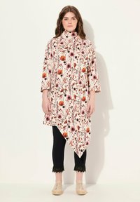 Bloemmotief tuniek in creme, met een hoge kraag en een asymmetrische zoom. Gecombineerd met zwarte crop pants met kant aan de zoom.