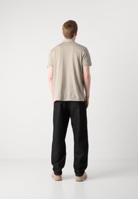 Polo-shirt i lys beige, kort erm, myk stoff. Kombinert med løstsittende mørk denim bukser og beige fottøy, sett fra bak.
