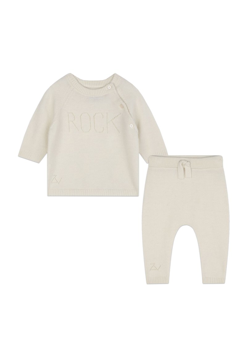 Creme gebreide trui met het woord "ROCK" in reliëf, voorzien van zijknopen; gecombineerd met bijpassende creme gebreide broek met elastische tailleband en opgerolde pijpen.