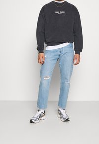 Mörkgrå crewneck sweatshirt med vit text; ljusblå rivna jeans; silver- och svarta sneakers. Avslappnad klädkombination.