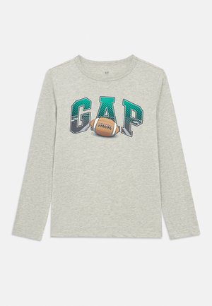 Cămașă gri deschis cu mâneci lungi, cu textul „GAP” în verde și negru și un grafic maro cu o minge de fotbal american în centrul pieptului.