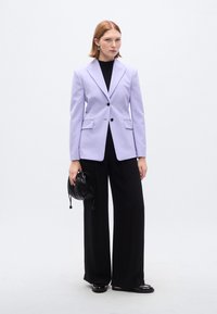 Λιλά σακάκι με δομημένο σχέδιο, μαύρα κουμπιά, δύο μπροστινές τσέπες, σετ με φαρδιά μαύρη παντελόνα και μαύρη τσάντα με κορδόνι.