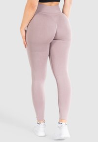 Leggings a vita alta in morbido tessuto mauve, con una finitura liscia e cuciture minime, abbinate a scarpe da ginnastica bianche.