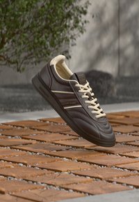 Brauner Ledersneaker mit hellcremefarbenen Akzenten und Schnürsenkeln. Verfügt über drei horizontale Streifen und eine strukturierte Sohle. Klassisches Design mit Logodetail.