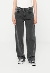 Bredde ben svarte denimjeans med en falmet vask, med frontlommer og knappelukking. Kombinert med svart-hvite kanvas sneakers.