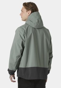 Světlá šedá nepromokavá bunda s kapucí, která má černý dolní lem a manžety. Hladká textura s minimem švů.