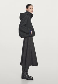 Zwarte gewatteerde jas met een capuchon, gedragen over een lange, geruite grijze rok, in combinatie met zwarte kniehoge laarzen. Eenvoudige, gestructureerde silhouet.