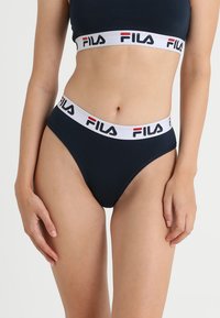 Námořnické modré bikini kalhotky vyrobené z hladké látky, s bílým elastickým pasem s logem "FILA" a červenými detaily.