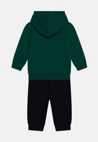 Sudadera verde con capucha y pantalones de chándal negros. Tejido de algodón, mangas largas, puños y cintura acanalados. Diseño simple de color sólido.