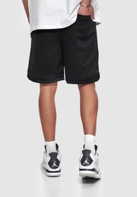 Sorte mesh sportshorts med sidelommer og løs pasform. Hvide strømper og sort/hvide sneakers med et logo på bagsiden.