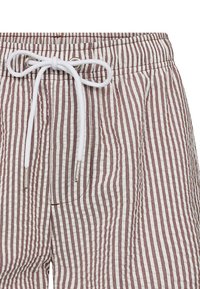 Striped shorts in white and burgundy, featuring an elastic waistband with a white drawstring and metallic aglets, showcasing a textured fabric.