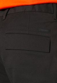Pantaloni neri Calvin Klein visti da dietro, dotati di una singola tasca posteriore con design piatto e una piccola etichetta del marchio sulla tasca.
