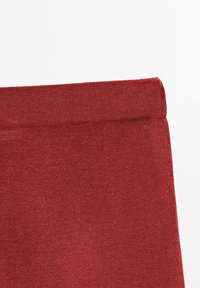 Gros plan d'un bord plié sur un vêtement en tissu tricot rouge, montrant des coutures fines et la texture sur un fond blanc.