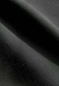 Fekete anyag, amely puha, texturált felületű, finom fénylával bír, és lágy redők találhatók rajta. Nem láthatóak minták vagy hardver.