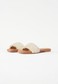 Des sandals à lanières ouvertes avec un dessus en tissu texturé crème, présentant un design duveteux, et une semelle intérieure en cuir marron lisse.
