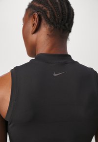Top atlético sin mangas negro con un cuello alto, que presenta un sutil logo de Nike en la parte posterior y costuras de hombro curvadas. Textura suave.