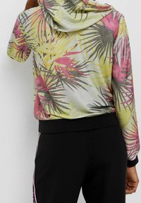 Kleurvolle hoodie met een tropische palmbladprint in roze, geel en groen. Zachte stof met een glanseffect; voorzien van een trekkoordcapuchon en zwarte manchetten.