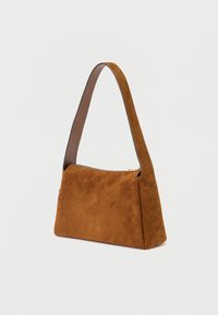 Malá hnědá semišová crossbody taška se širokým popruhem a zlatým zipem na bílém pozadí.